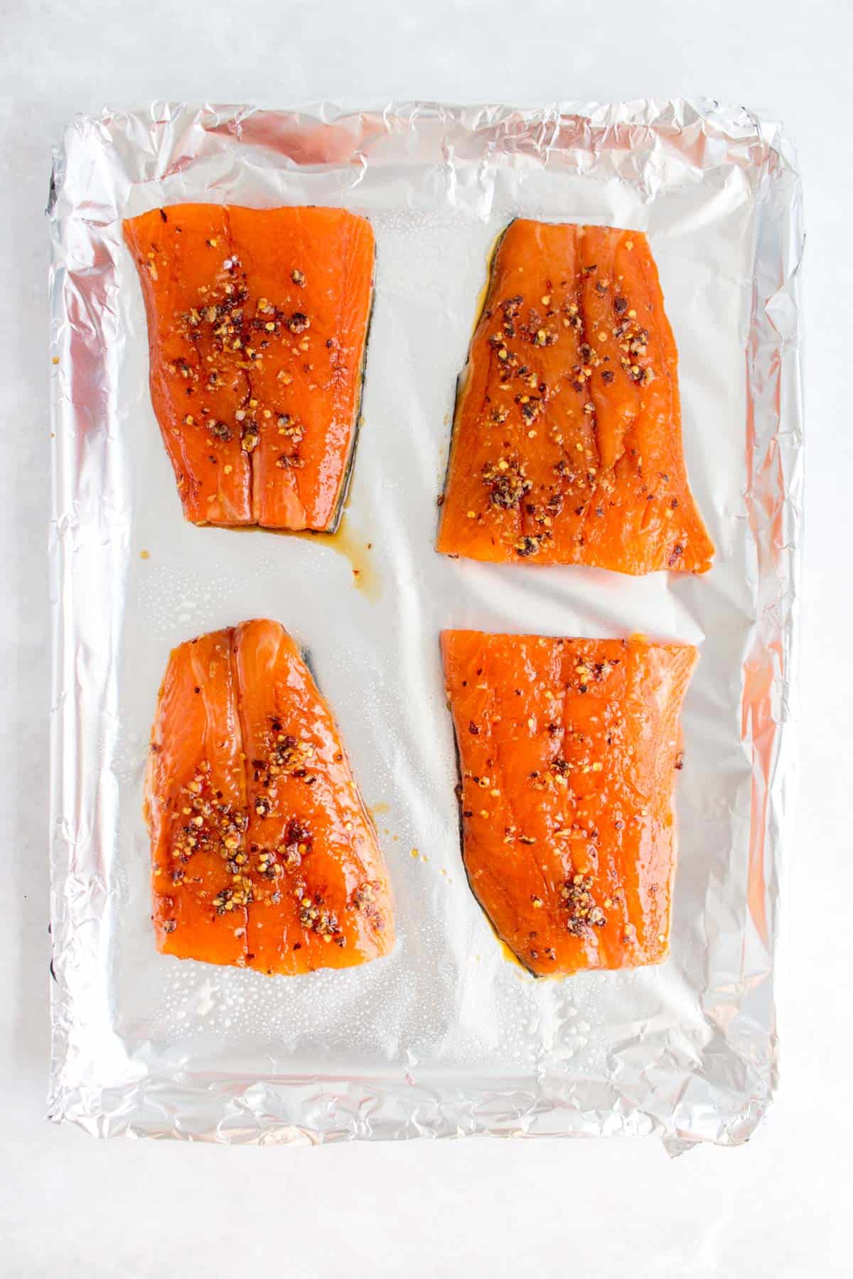 Four salmon fillets on a sheet pan.