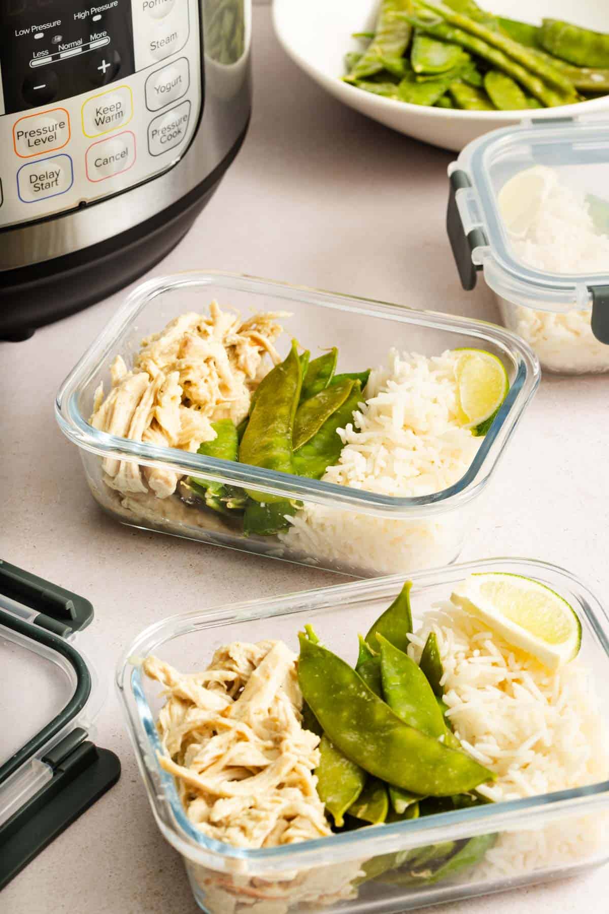 Two meal prep containers with thai coconut curry chicken, snow peas, and rice beside an Instant Pot.
