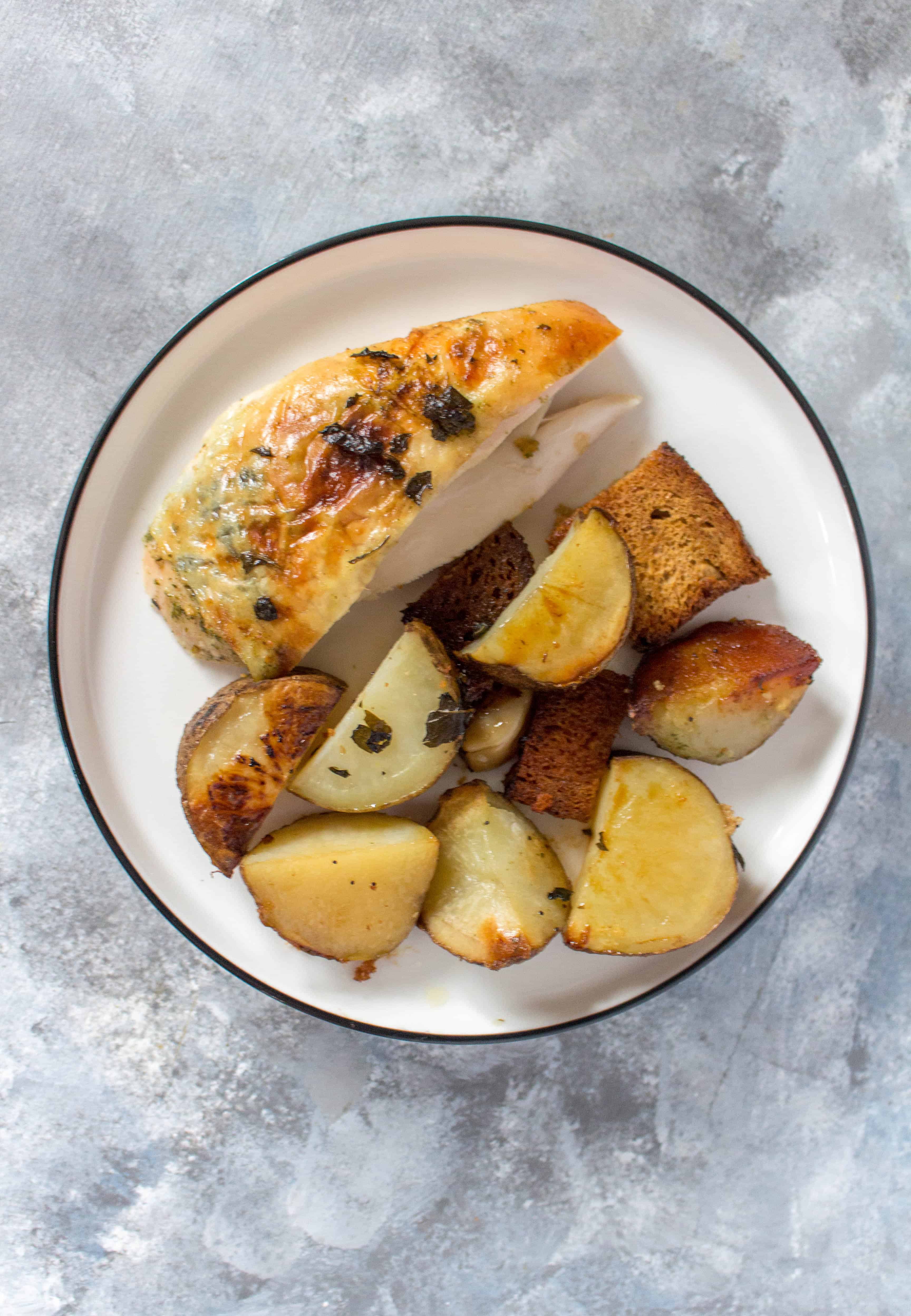 A plate with a slice of dutch oven roasted chicken with potatoes and crispy bread.