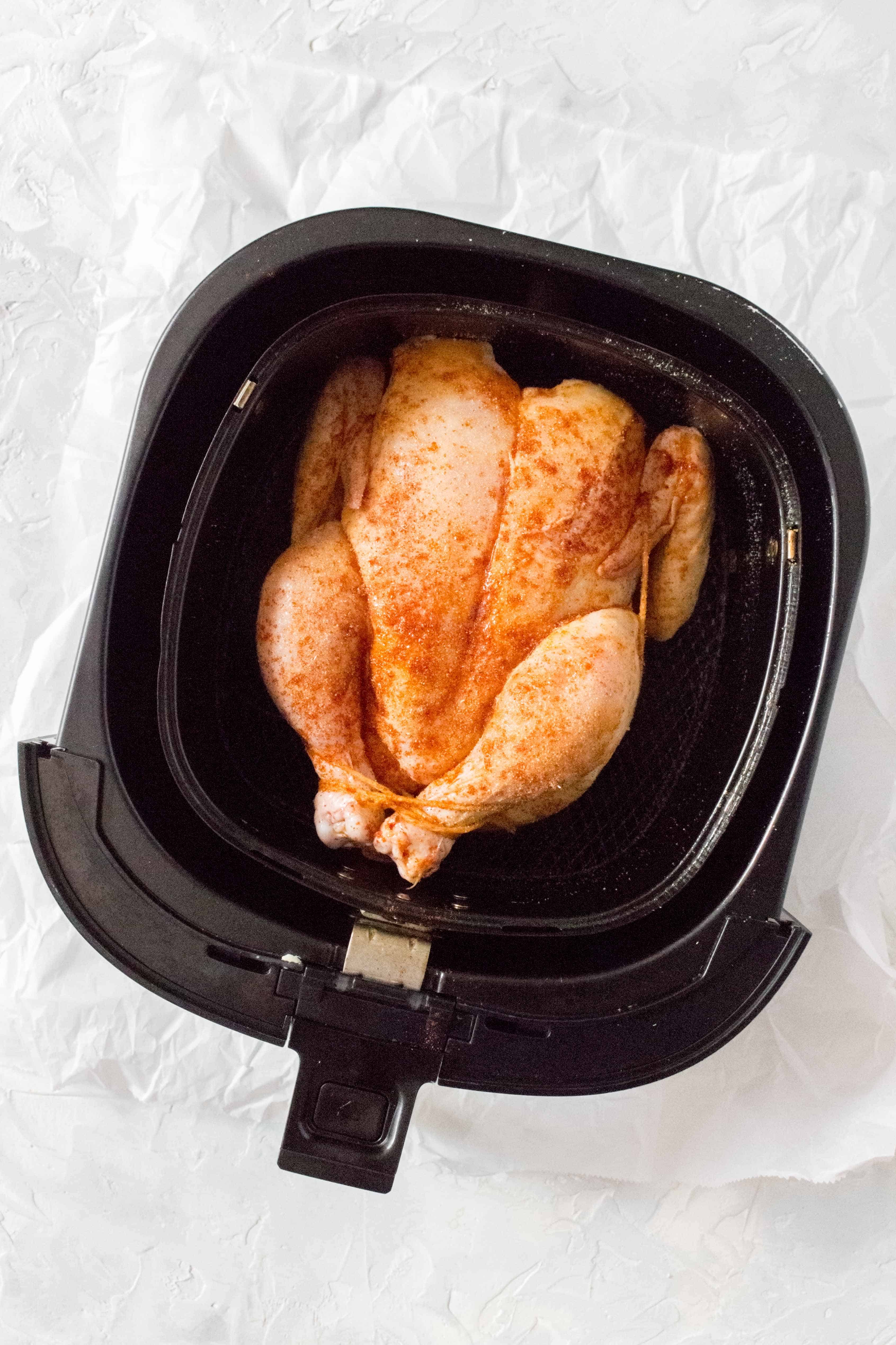 A seasoned raw whole chicken inside of an air fryer basket.