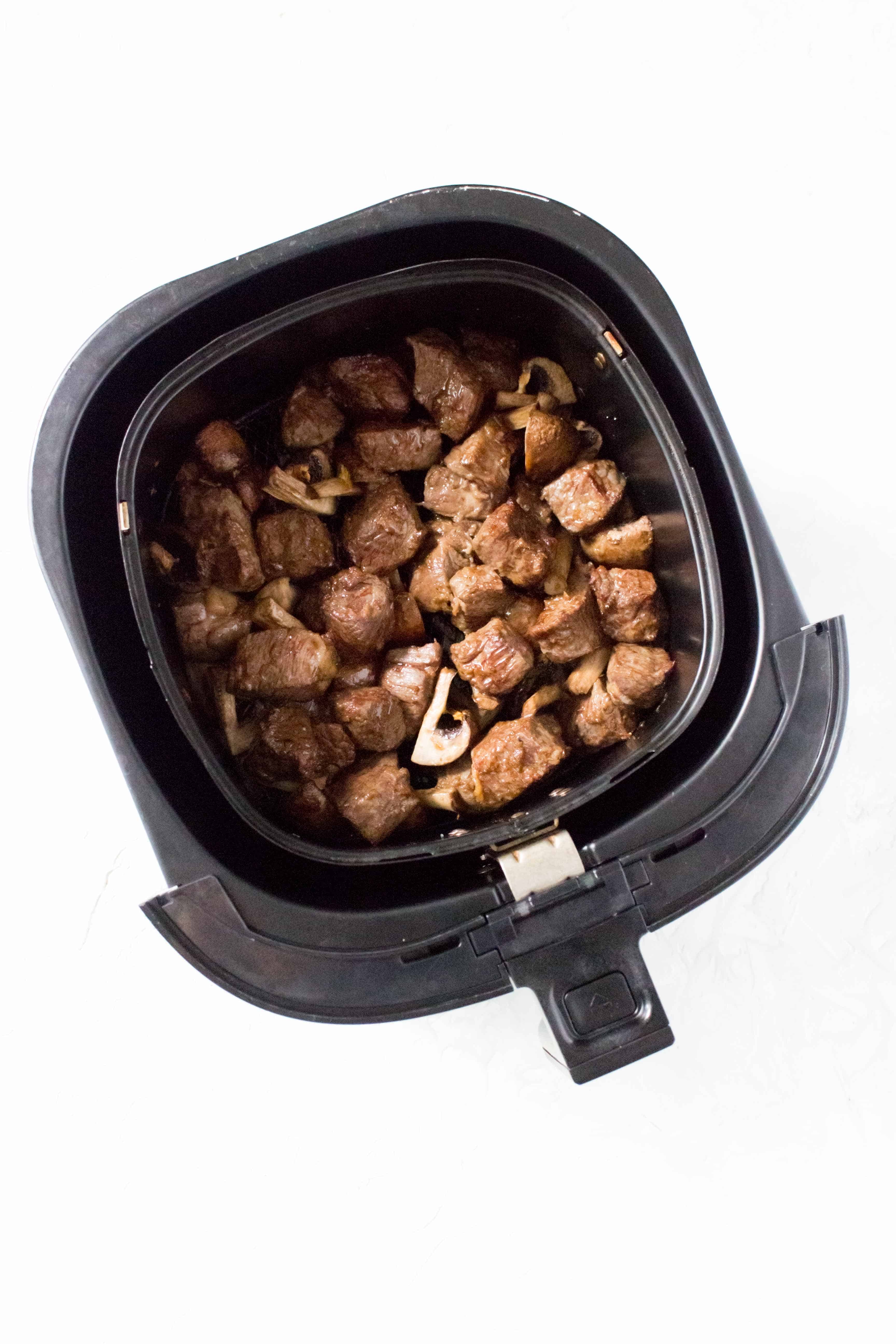 Overheat view of air fried steak bites and mushrooms in an air fryer basket.