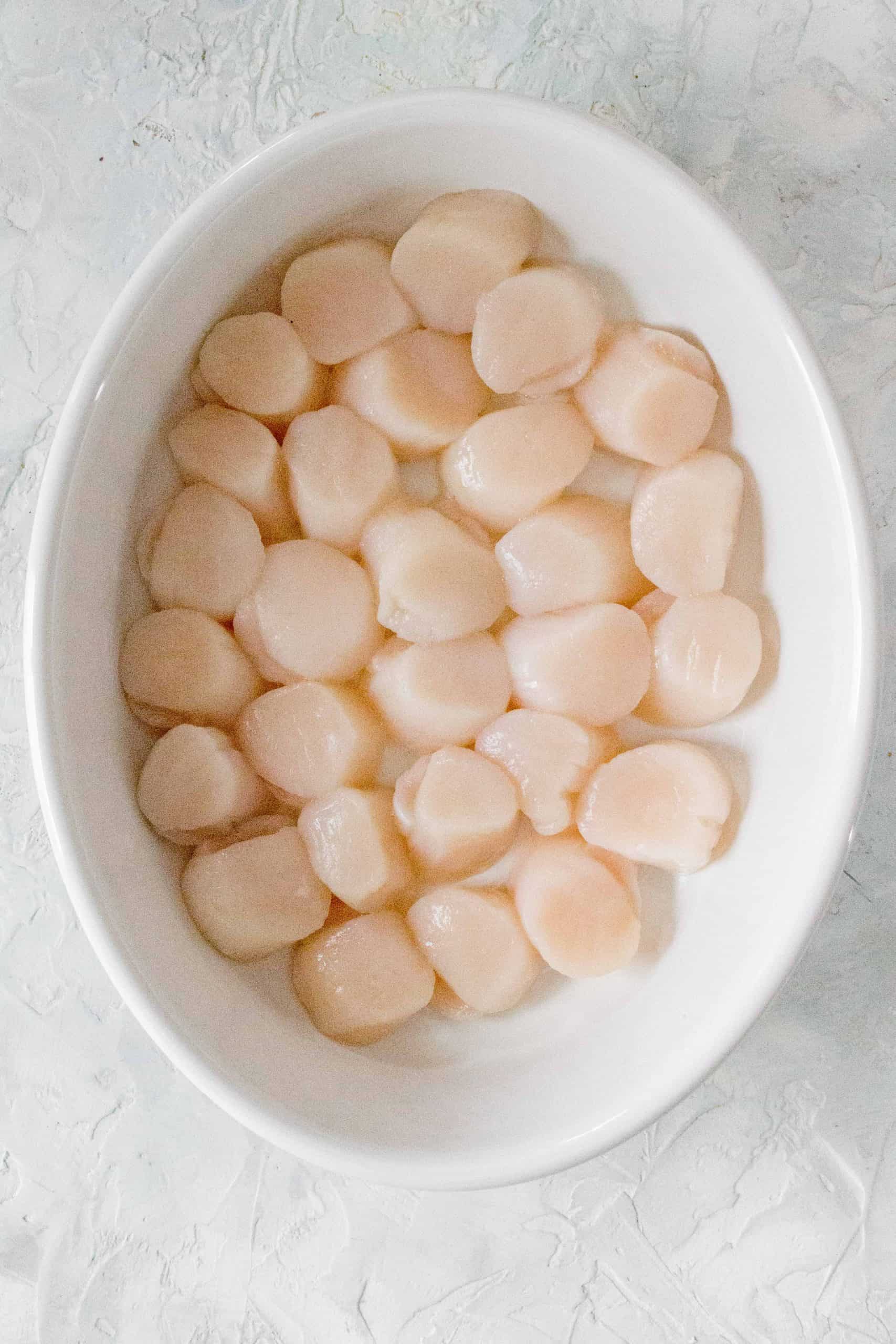 In a baking dish, line your scallops up in a single layer before pouring the butter mixture over the sea scallops.