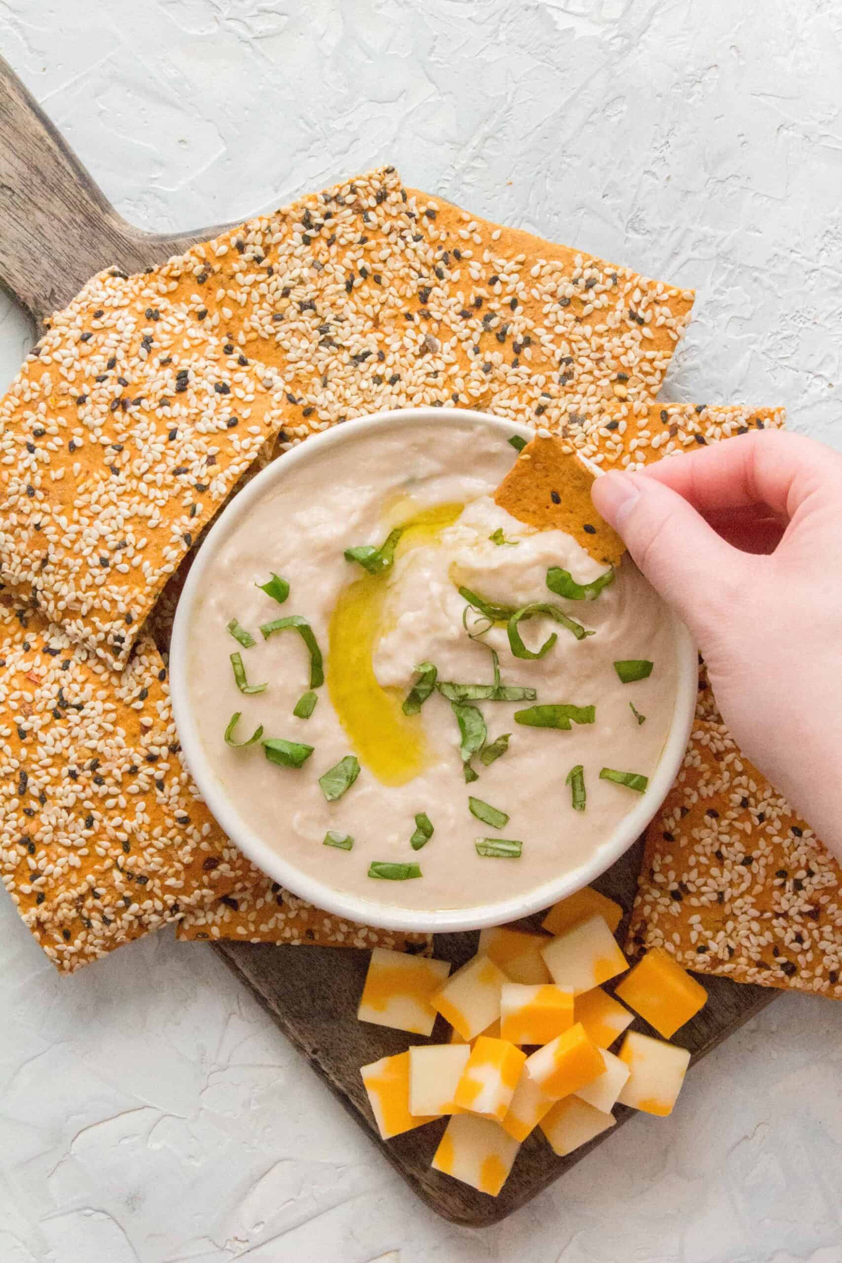 white bean hummus dip surrounded by crackers and cheese.