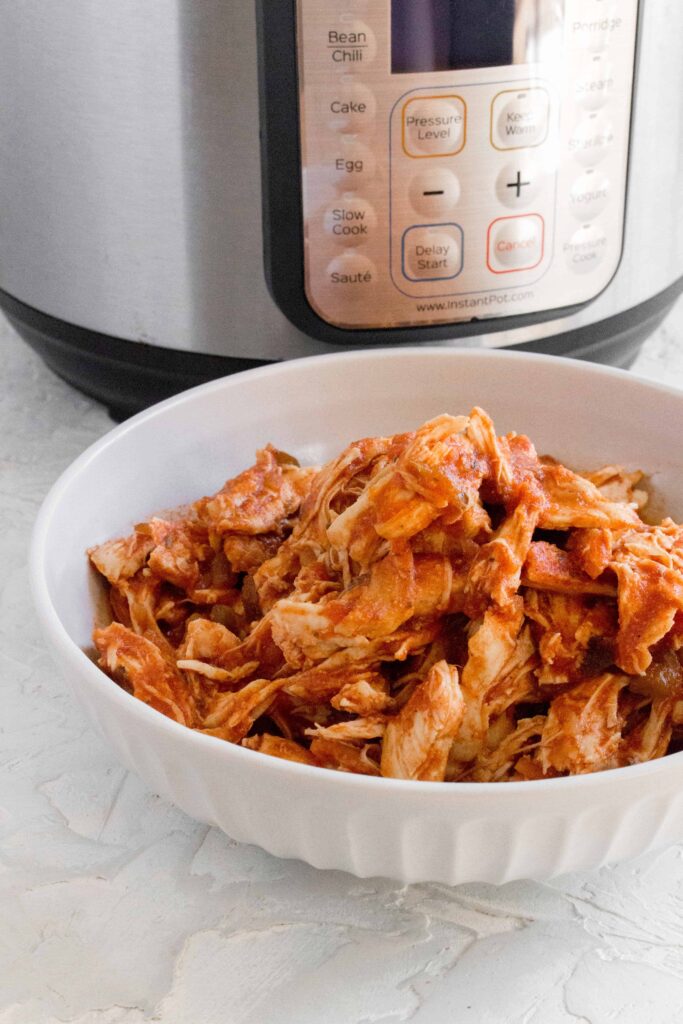 bowl of shredded salsa chicken in front of the Instant Pot