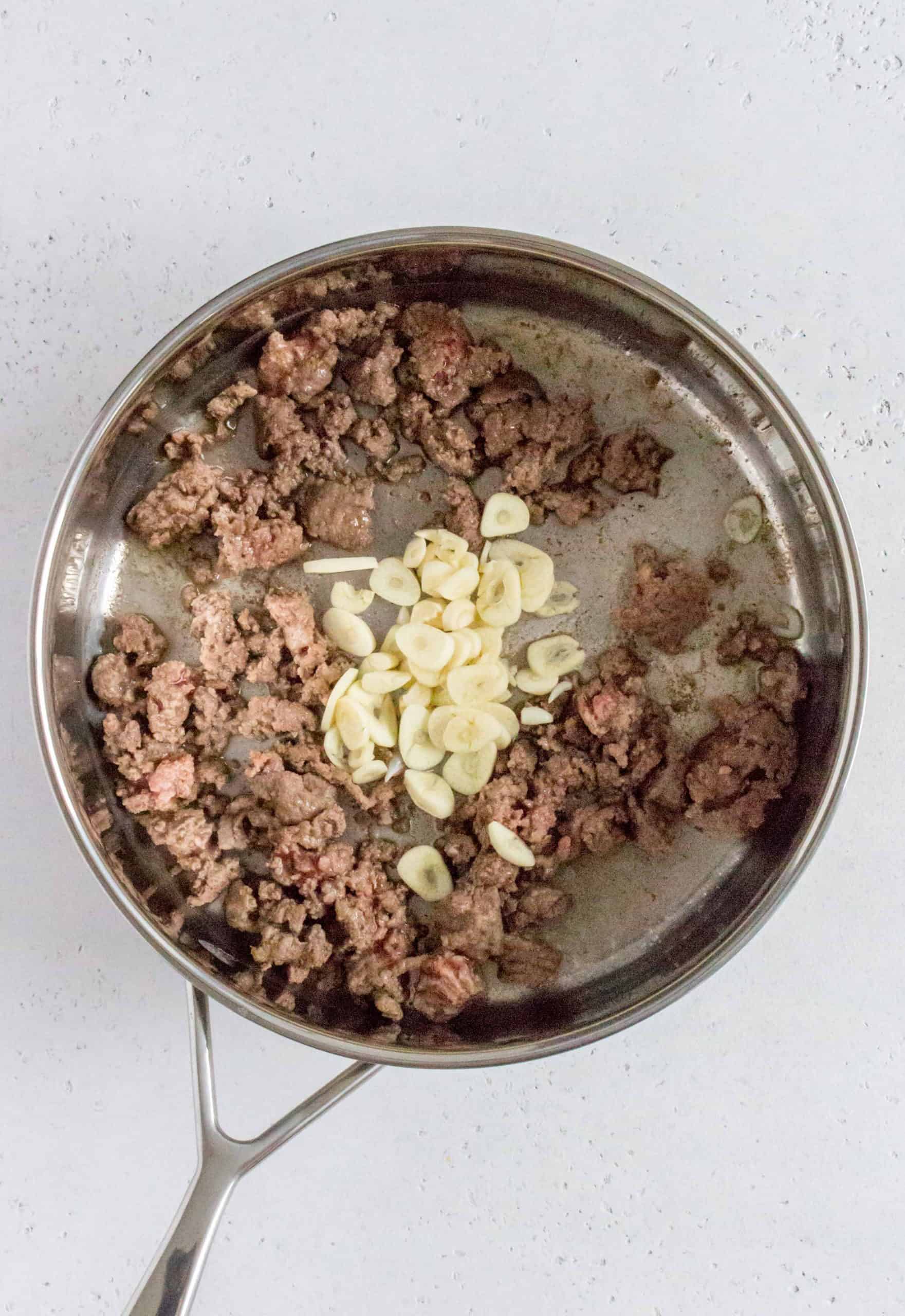 While the water is boiling, in a medium sized pan, melt your butter and start browning your ground beef, breaking it up with a wooden spoon as you go along. Once mostly, browned, add in the garlic and sauté.