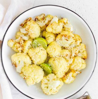 Plate with roasted cauliflower with 2 wedges of lime and a bit of parmesan on top