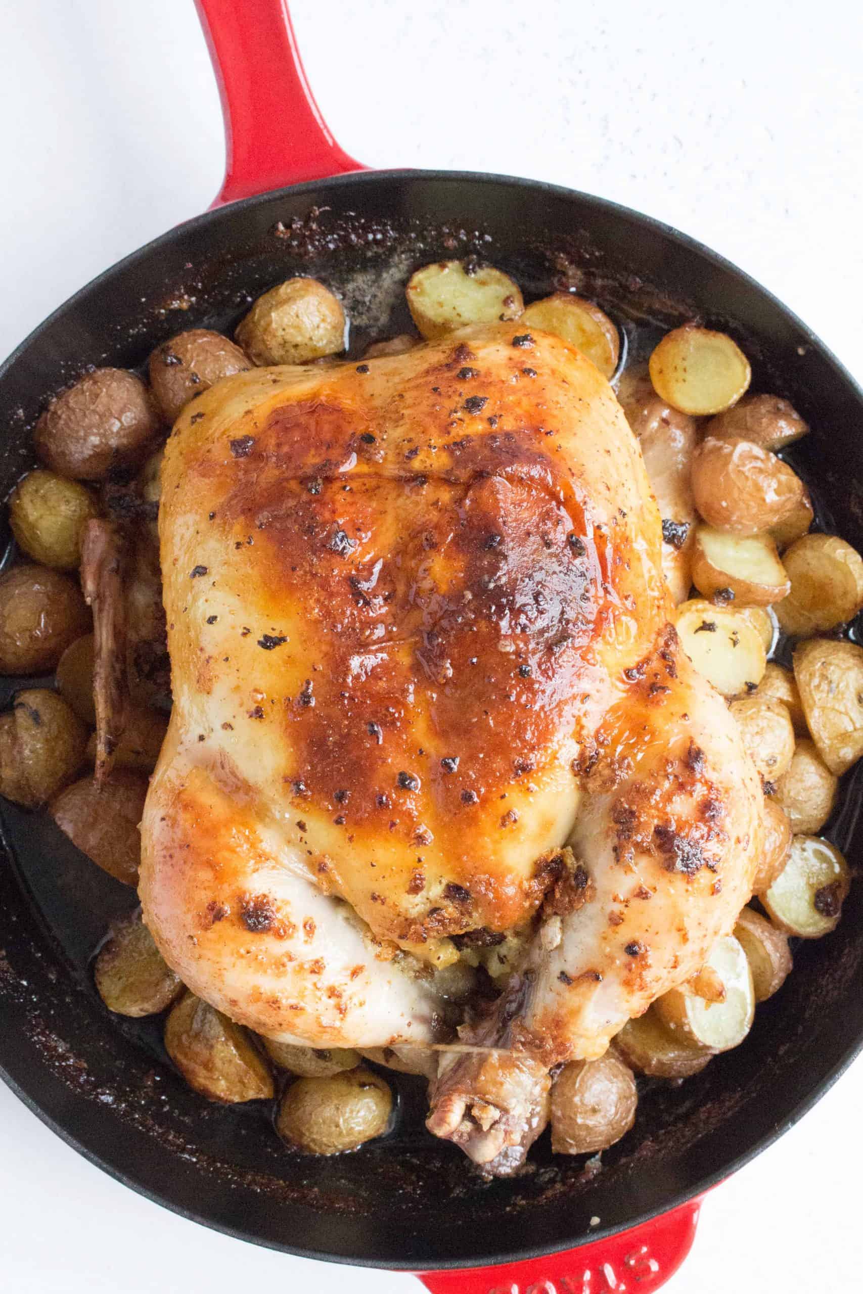 whole roast chicken inside a red cast iron skillet surrounded by baby potatoes