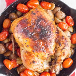 whole roast chicken in a cast iron staub skillet with baby potatoes and grape tomatoes