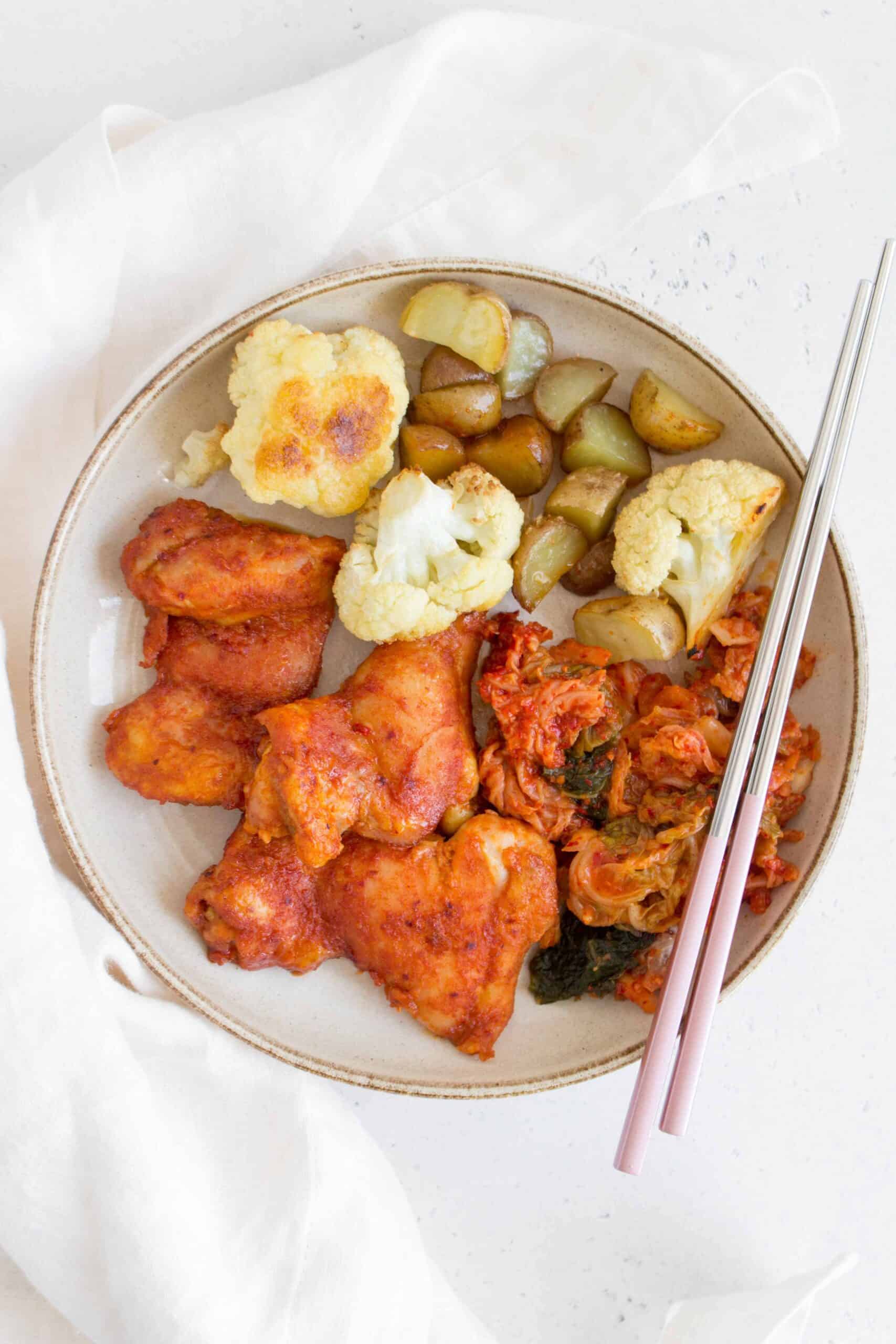 plate with spicy korean chicken thighs, roasted cauliflower, mini potatoes, and kimchi