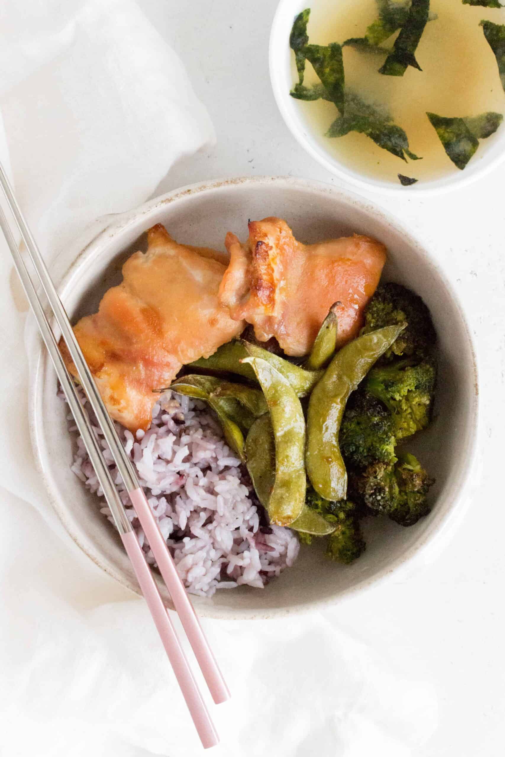 miso baked chicken thighs in a bowl with broccoli edamame and purple rice