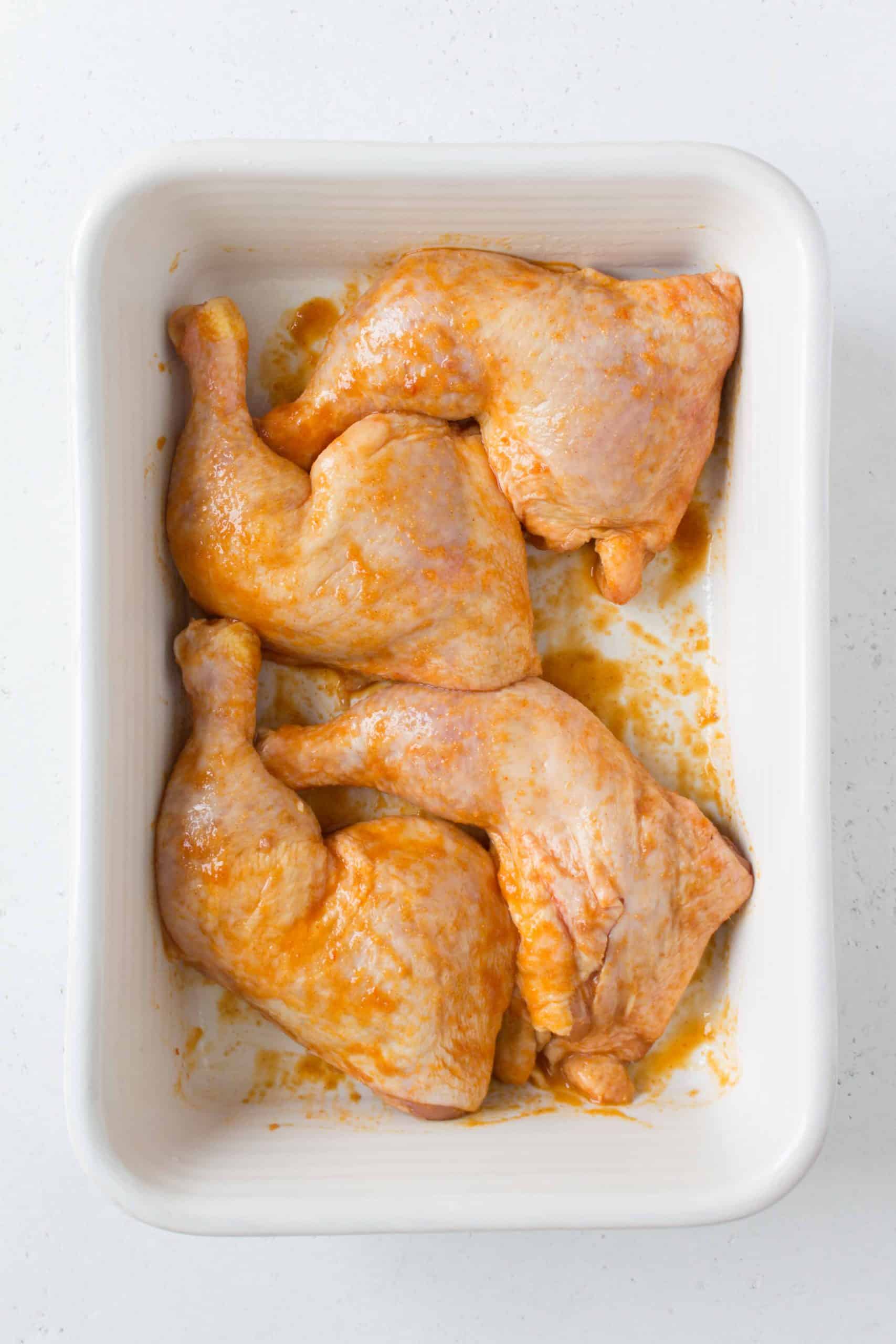 quartered chicken legs in a large white baking dish