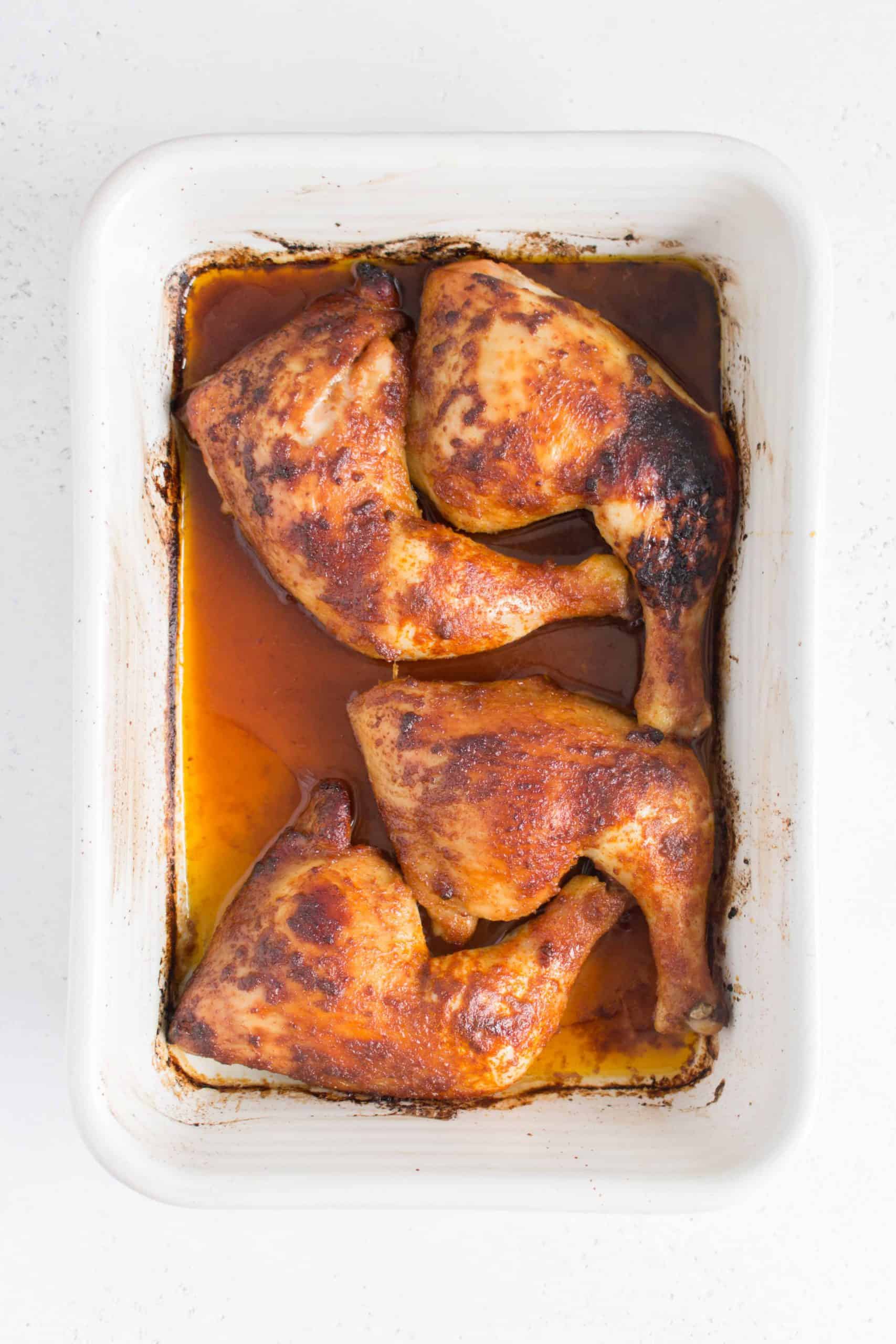 Overhead view of baked chicken quarters in a white baking pan.