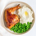 plate with a oven roasted chicken quarter with mashed potatoes and peas