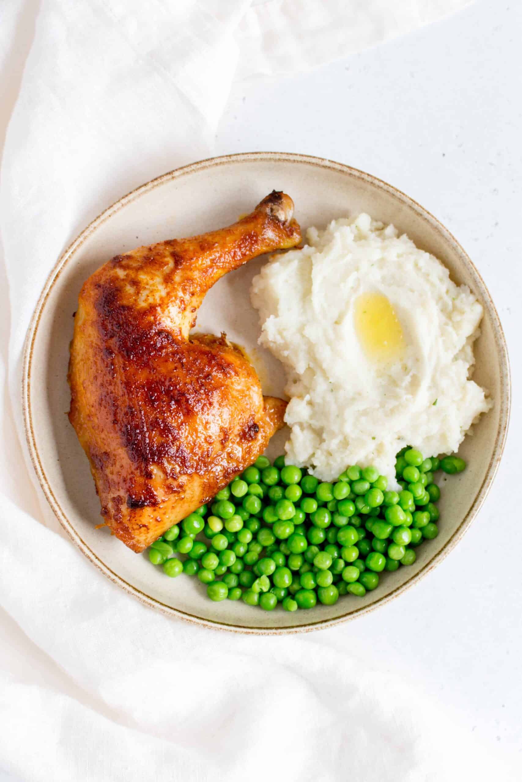 plate with a oven roasted chicken quarter with mashed potatoes and peas
