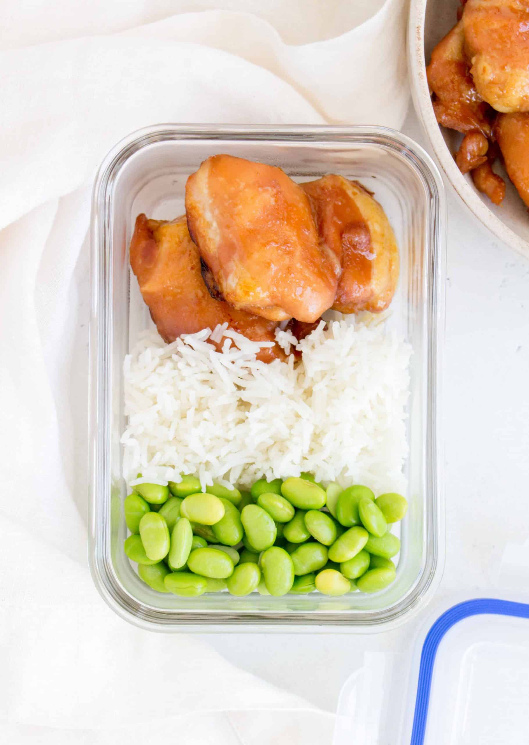 meal prep container containing honey soy chicken thighs, rice, and edamame beans