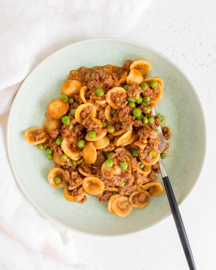 orecchiette pasta with beef and peas in a green plate with a black and silver fork