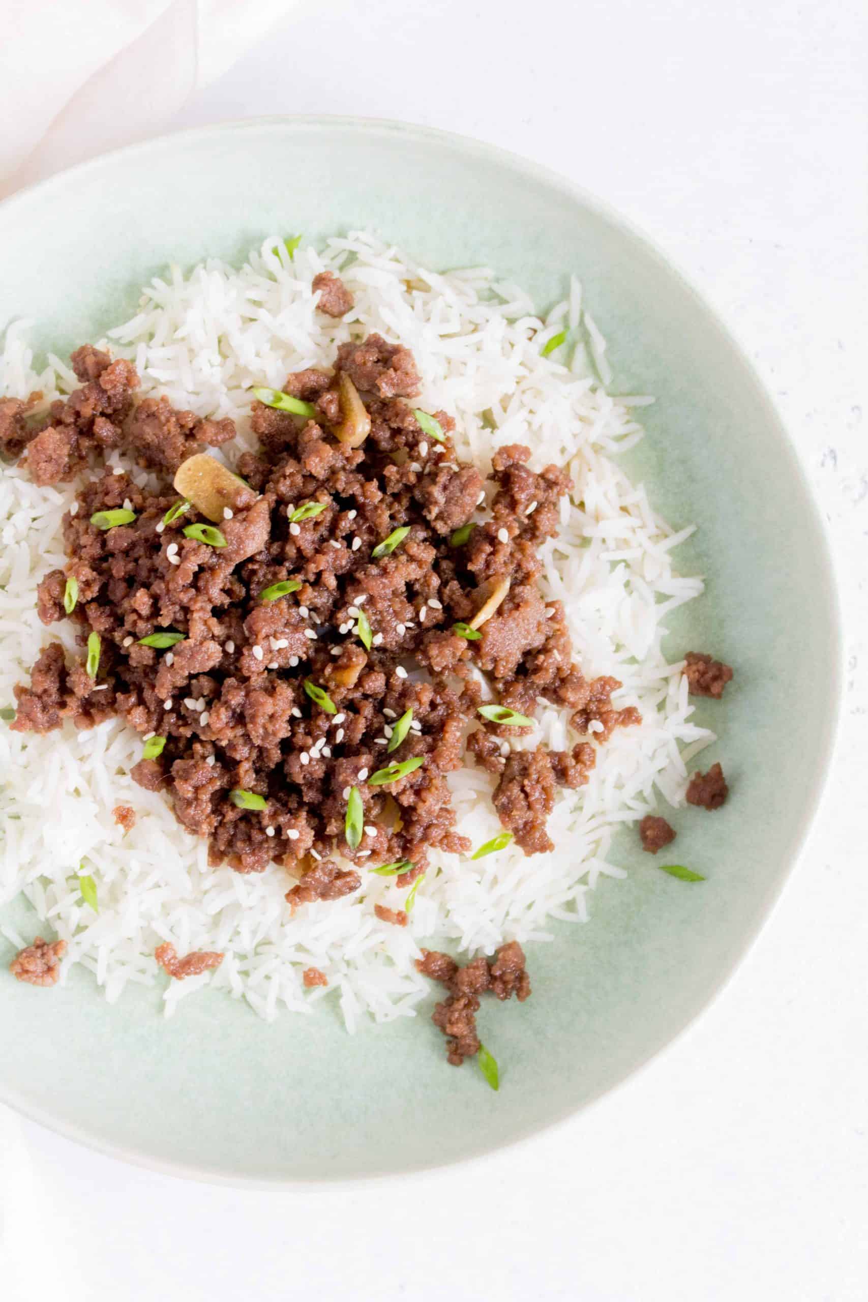 plate with rice and teriyaki ground beef on top with sesame seeds and green onions.