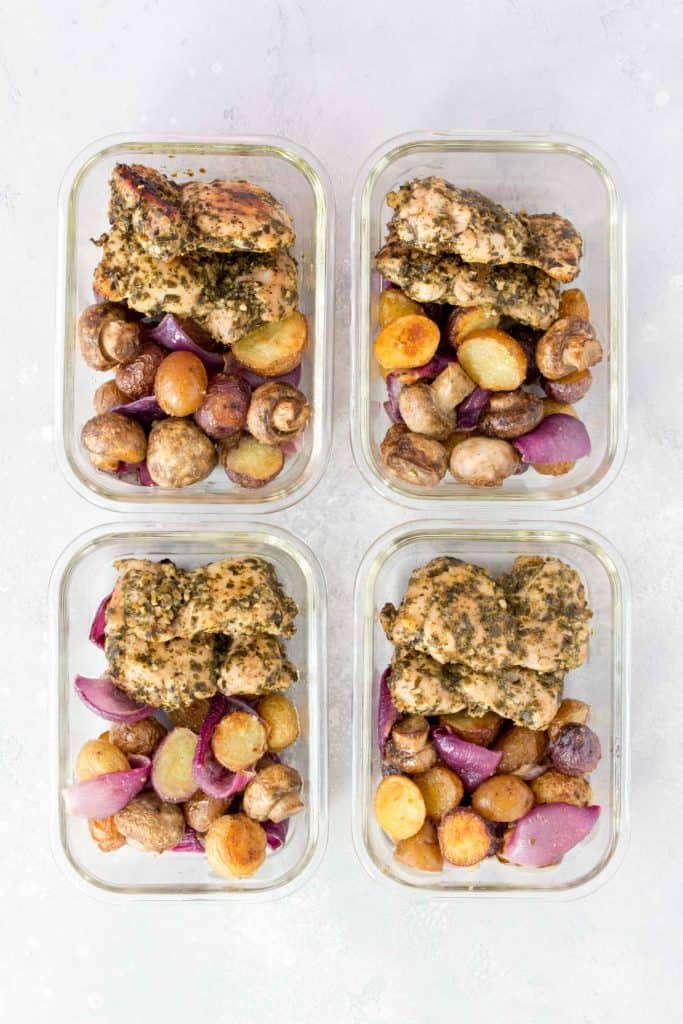 4 glass meal prep containers with pesto chicken thighs and potatoes, red onions, and mushrooms