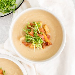 bowl of parsnip soup with pea shoots, bacon, and croutons on top