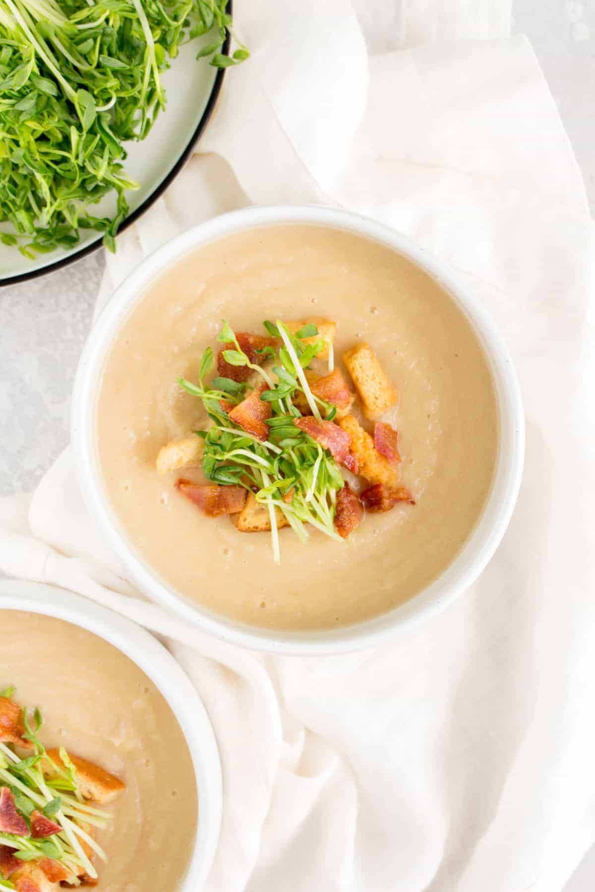 bowl of parsnip soup with pea shoots, bacon, and croutons on top