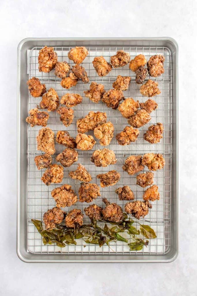 Sheet pan with wire rack cooling the freshly fried Taiwanese popcorn chicken and fried basils.