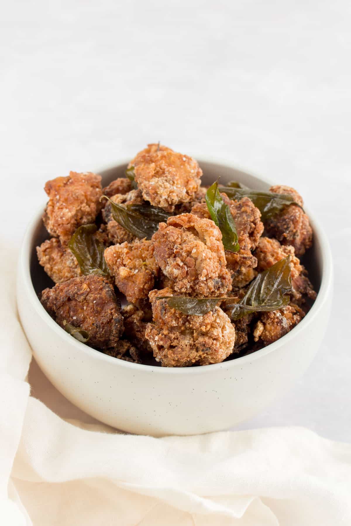 Angled image of a white bowl with Taiwanese Fried Chicken and fried Thai basil.