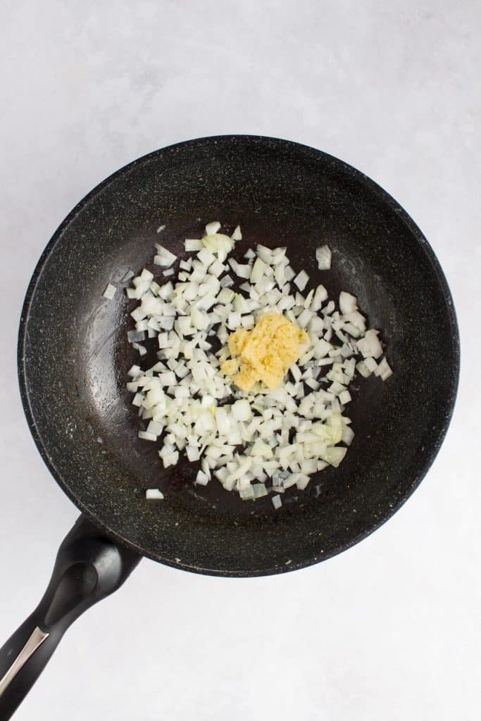 Instructional photo showing onions being sautéed with garlic in a wok.