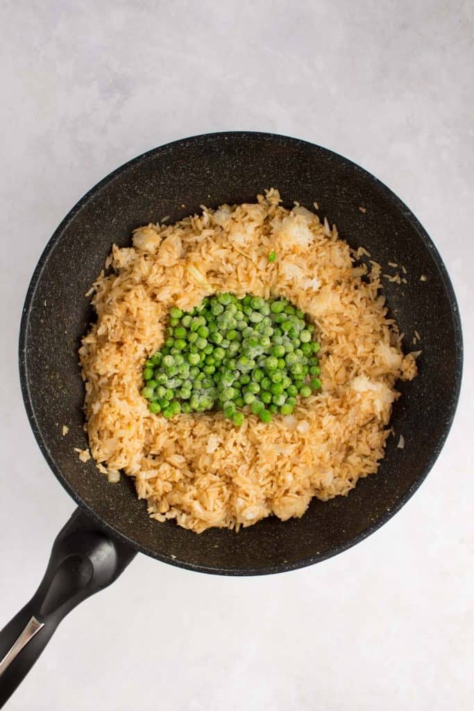 Instructional photo showing peas added to the fried rice in a wok.