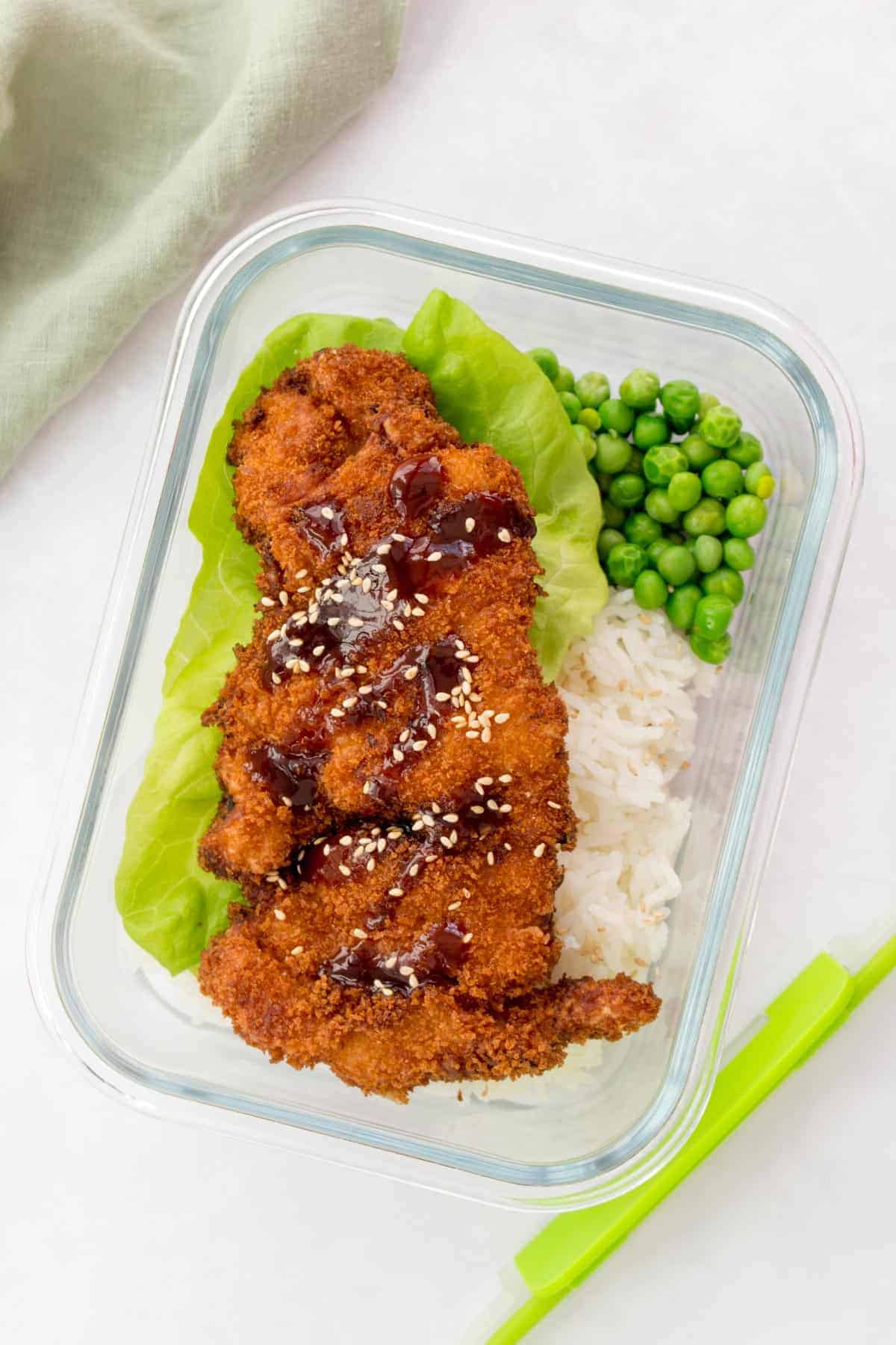 Chicken katsu in a bento box with rice, peas, and lettuce.