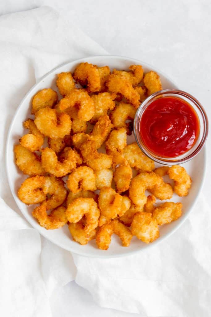 Breaded popcorn shrimp on a white plate with a serving of ketchup.