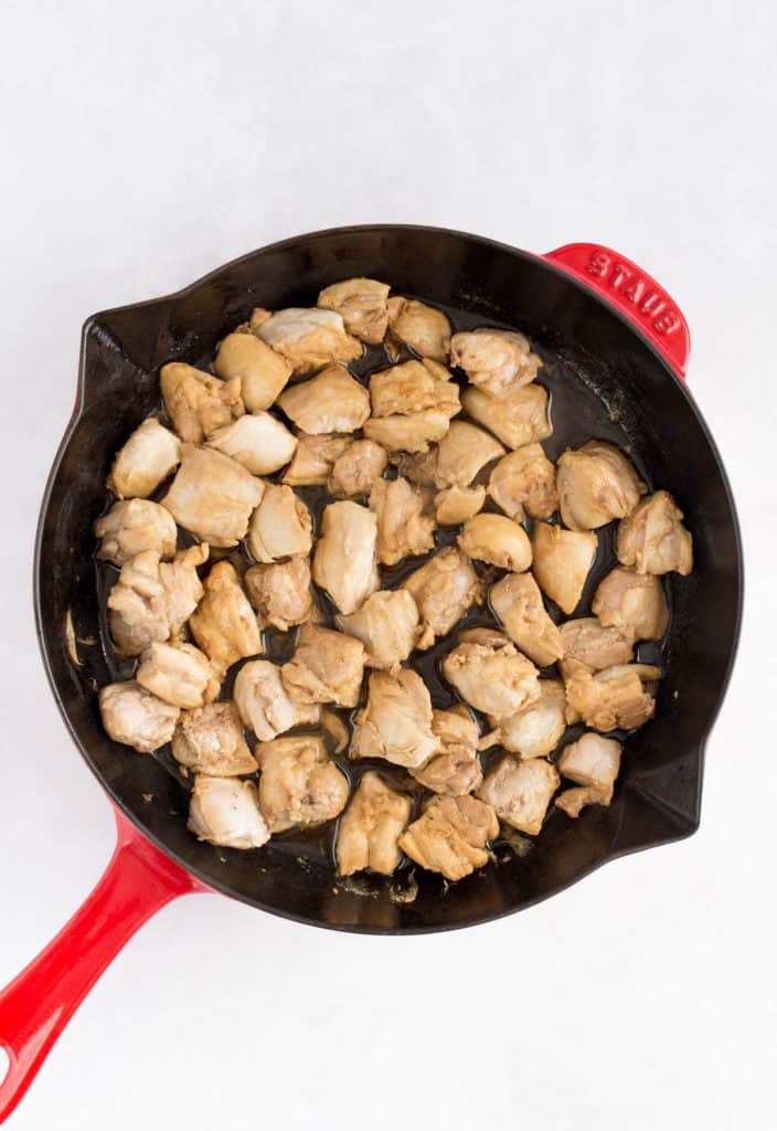 Diced chicken with sauce in a red skillet.