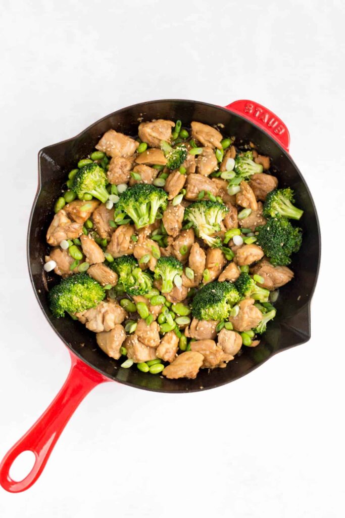 A red skillet with chicken and broccoli and edamame.
