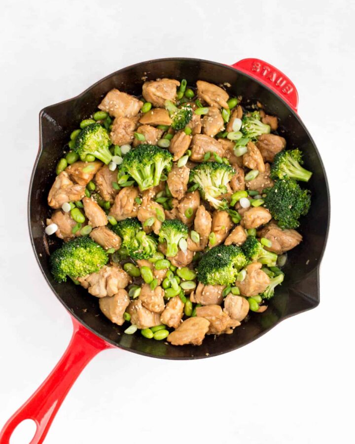 A red skillet with chicken and broccoli and edamame.