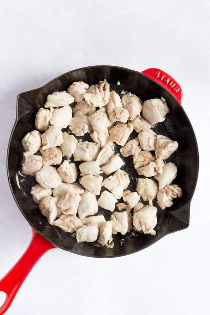 Diced chicken thighs in a red skillet.