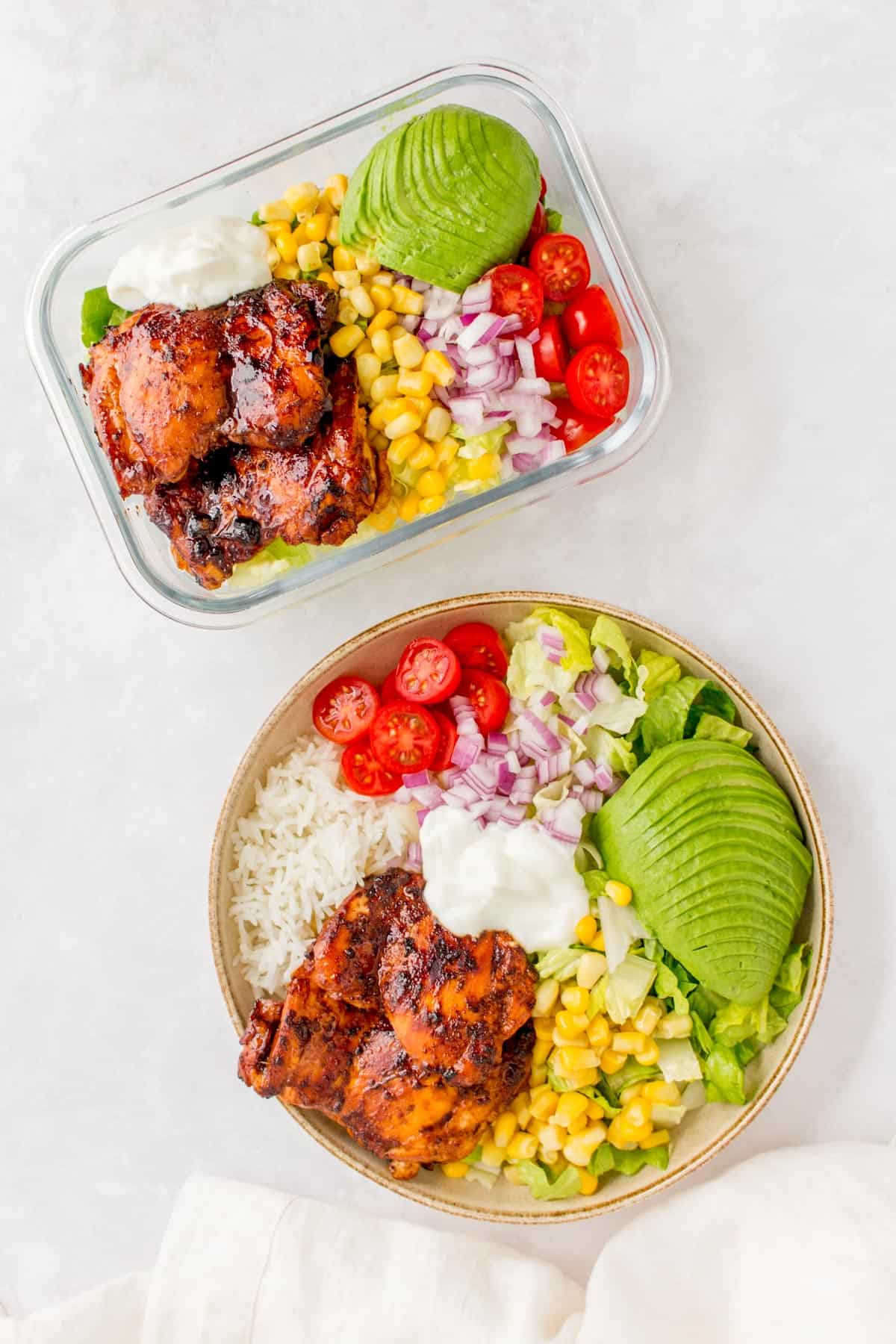 Overhead photo of a honey chipotle chicken salad in a meal prep container beside a burrito bowl.