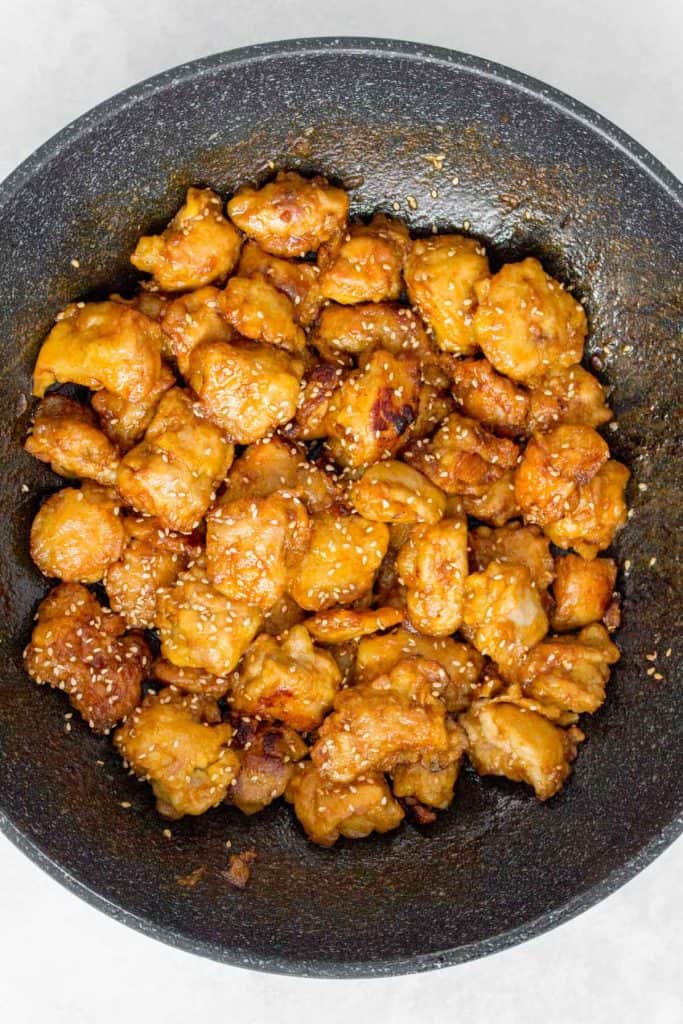 Sesame chicken in a skillet topped with sesame seeds.