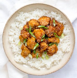 Sesame chicken over a bed of rice on a plate.