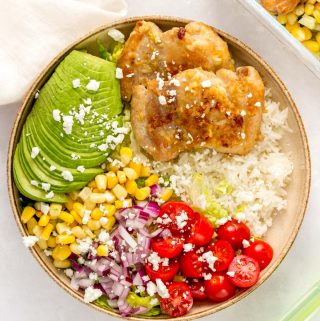 A plate with rice, lettuce, tomatoes, red onion, corn, avocado, and garlic butter chicken thighs.