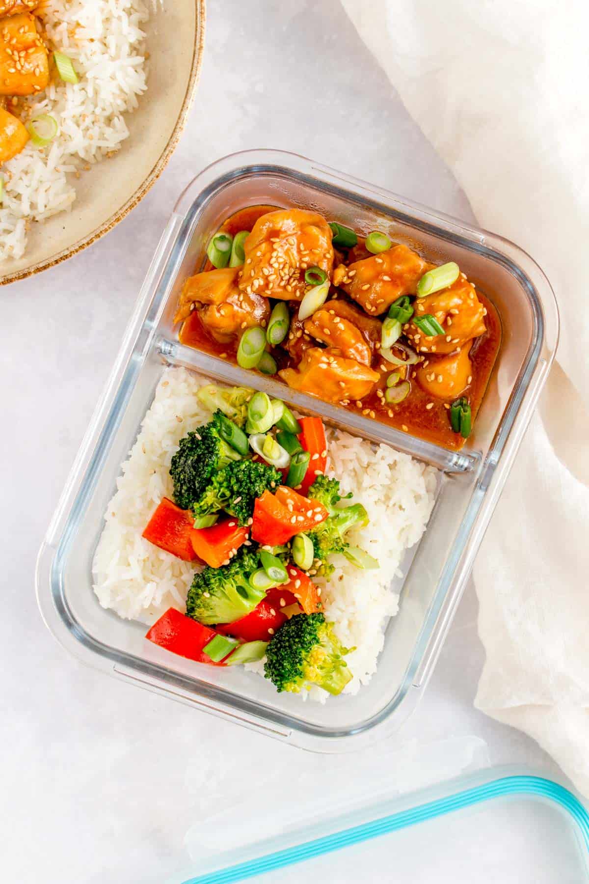 Meal prep container with sesame chicken and vegetables over rice.