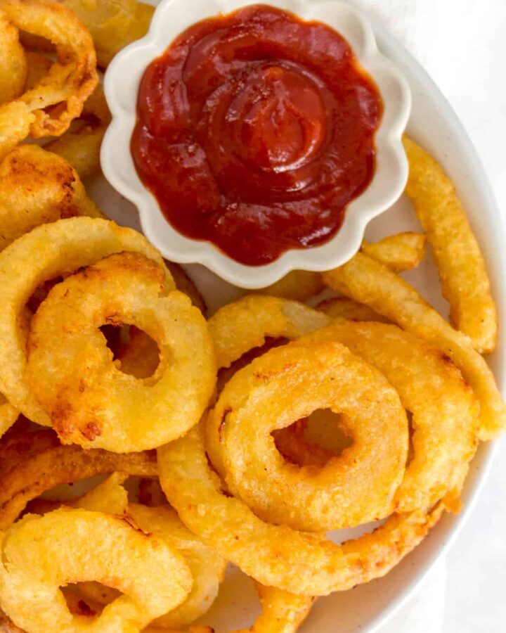Close up of onion rings on a plate beside ketchup.