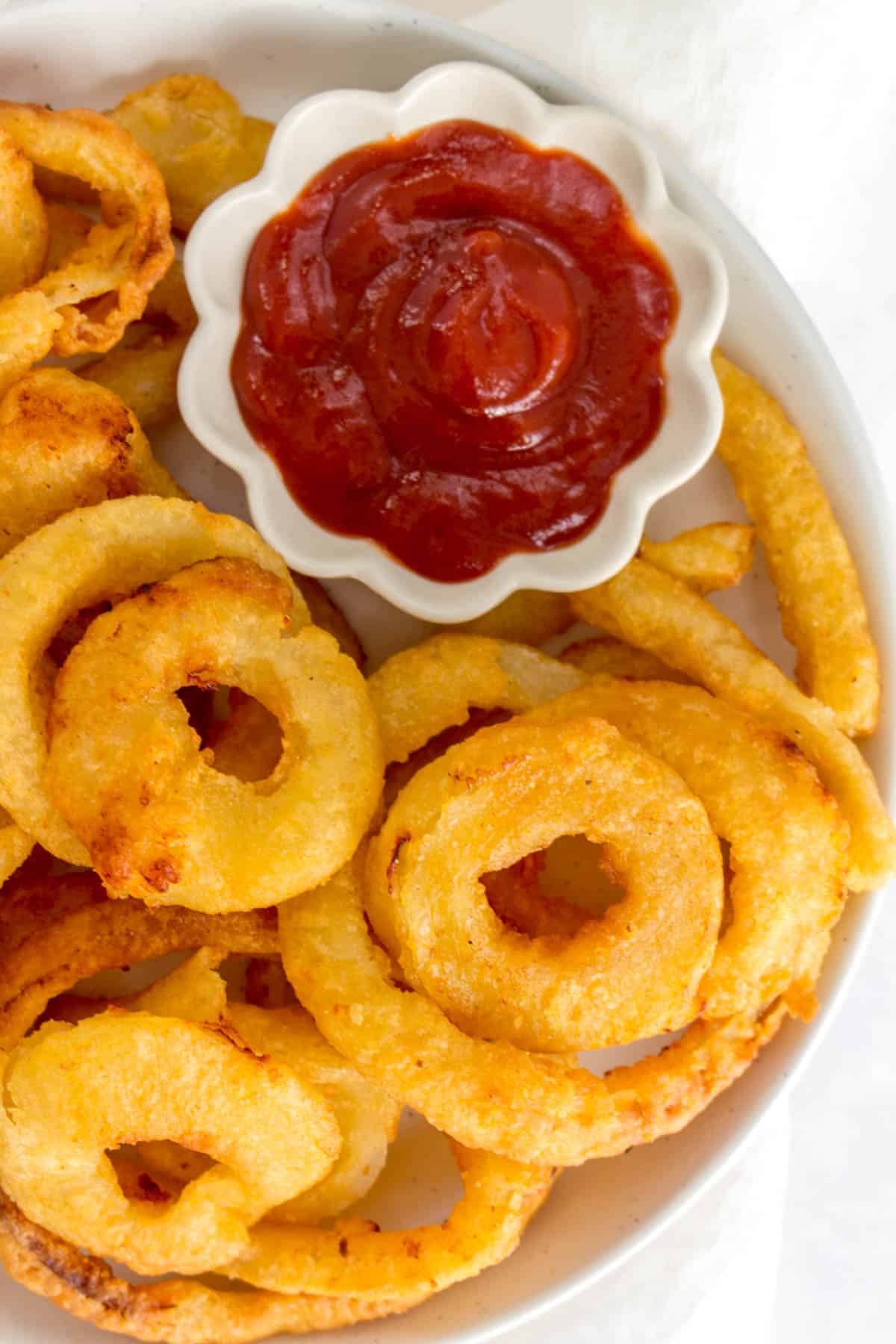 Close up of onion rings on a plate beside ketchup.
