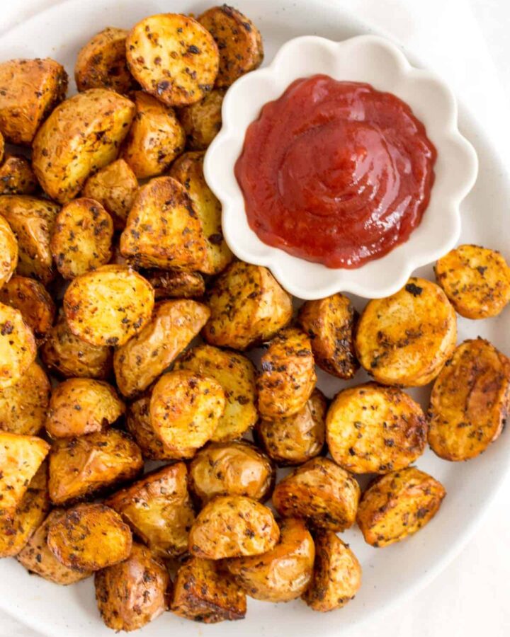 White plate of air fryer roasted potatoes with a serving of ketchup.