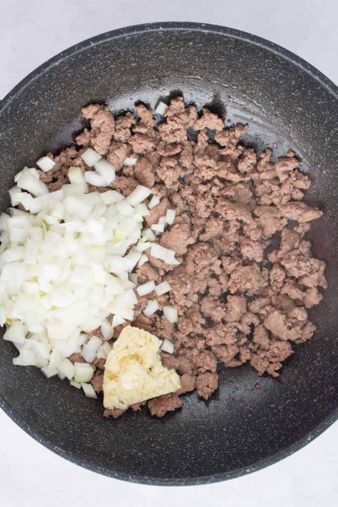 Adding diced onions and garlic to a pan with beef.