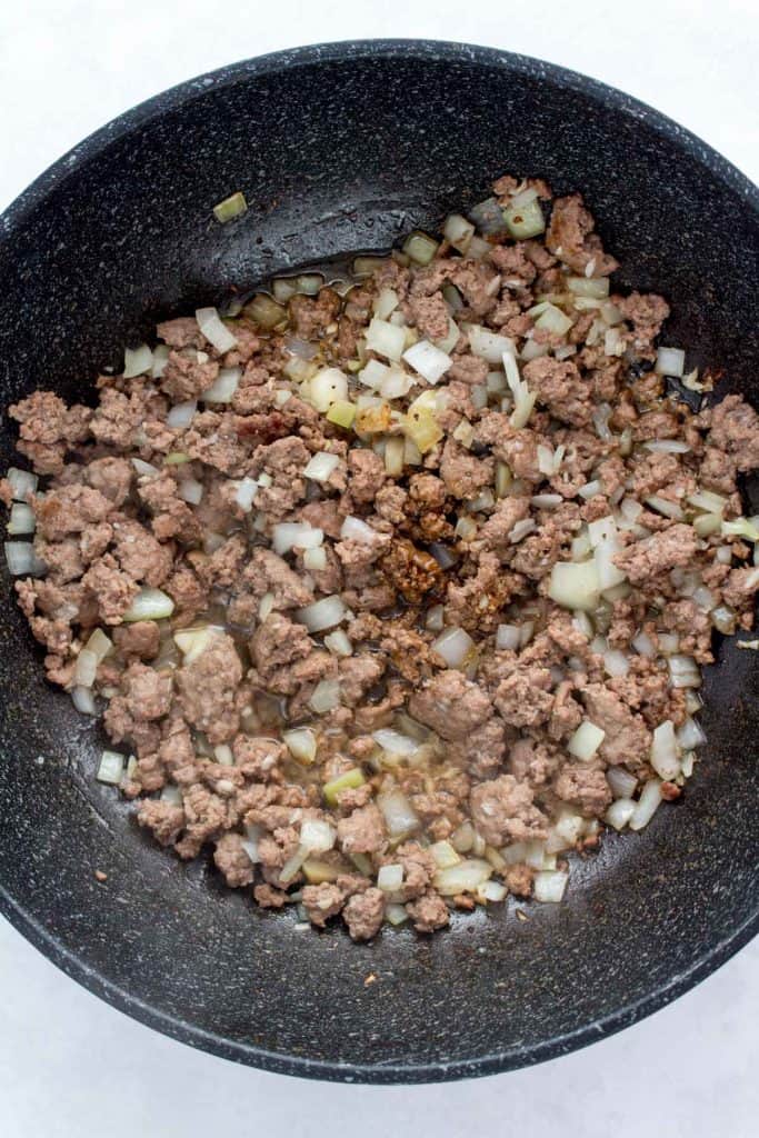 Adding sauce to a wok with beef, onions, and garlic.