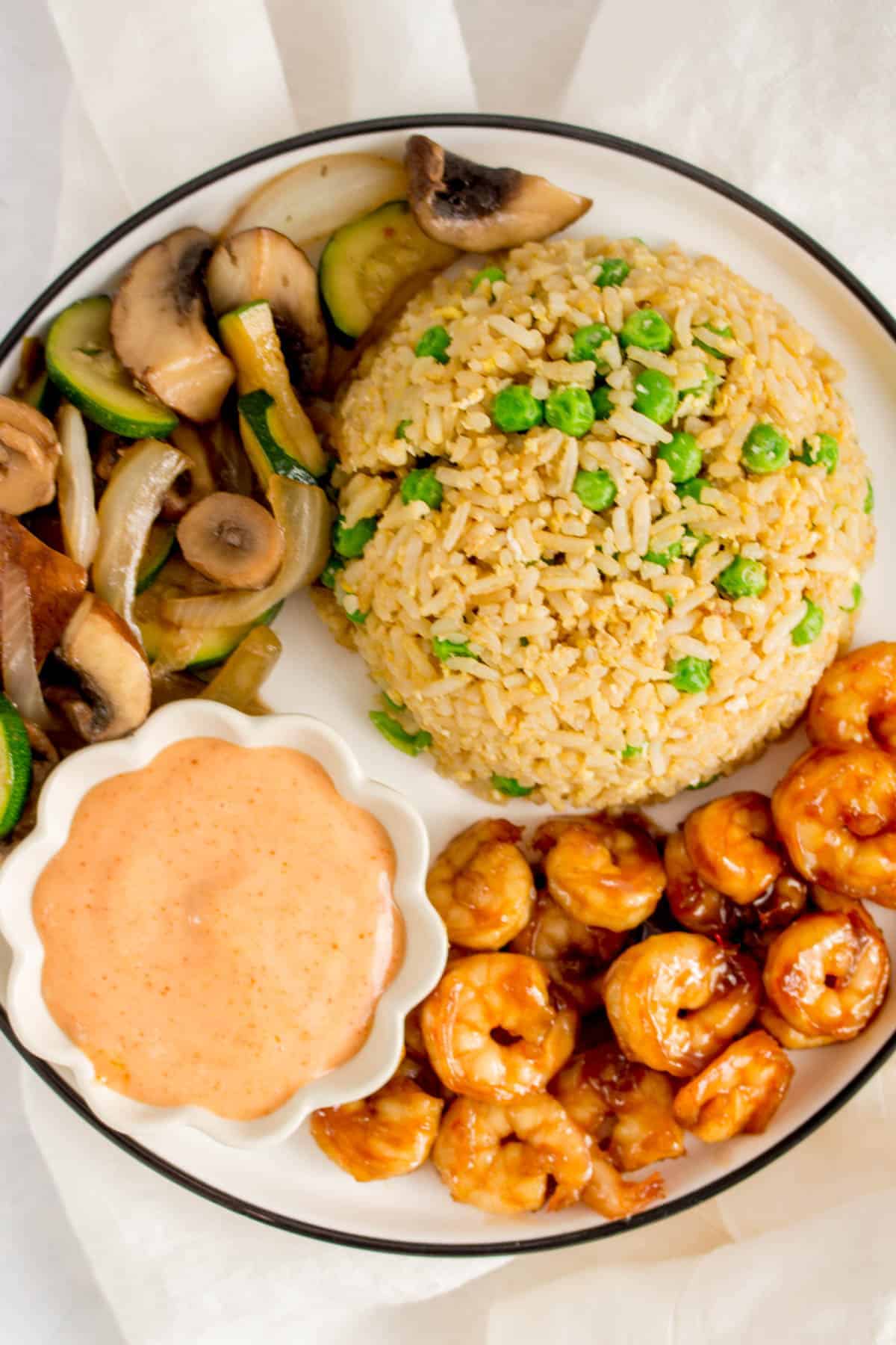 Close up of a plate of hibachi shrimp, vegetables, fried rice, and yum yum sauce.
