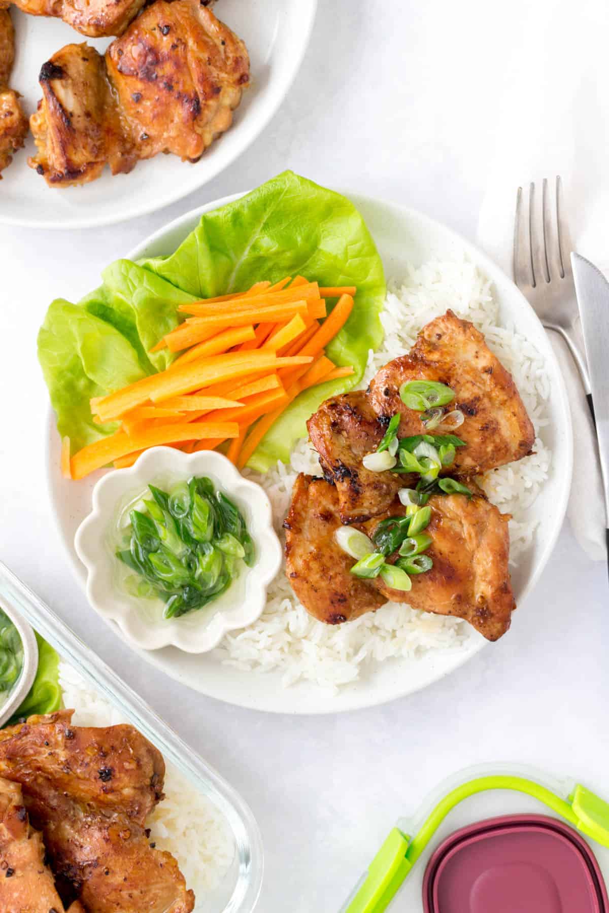 White plate with rice, lemongrass chicken, scallion oil, lettuce, and sliced carrots.