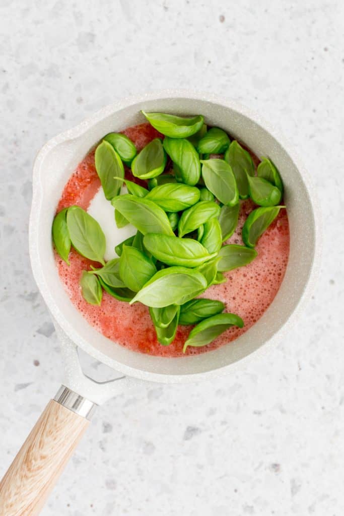 A pot with strawberry puree with sugar and basil in the pot.