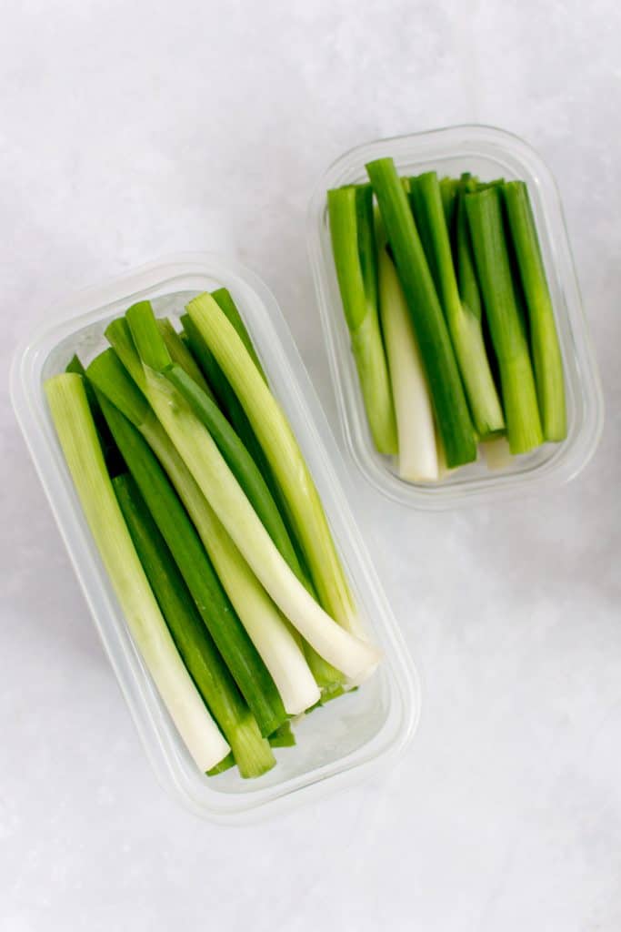 Green onions cut in half in a freezer container.
