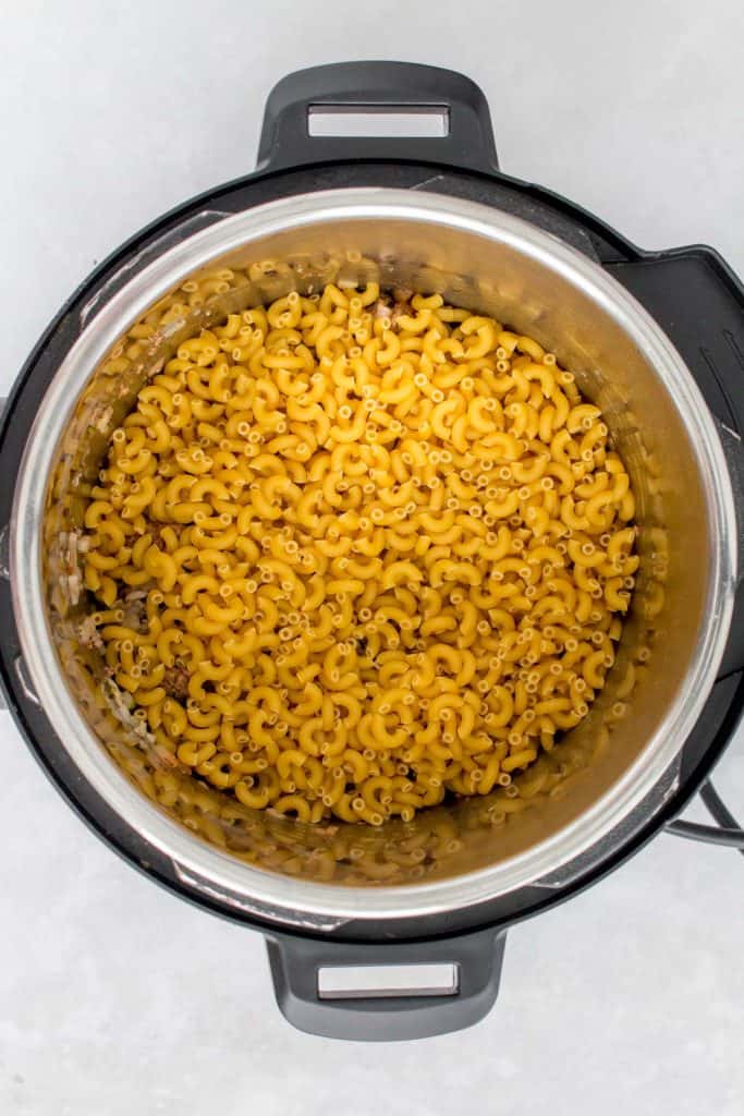 Macaroni being added to an Instant Pot liner for goulash.