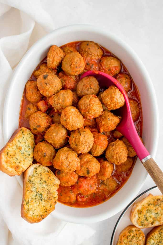 Serving platter of cooked meatballs with two pieces of garlic bread in the platter.